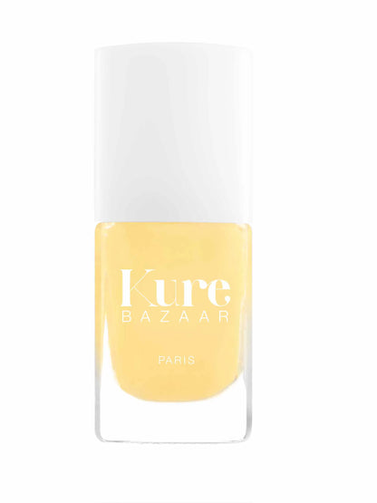 A bottle of Kure Bazaar Paris nail polish in a soft pastel yellow shade, featuring a white cap and a clear glass base, set against a plain white background.