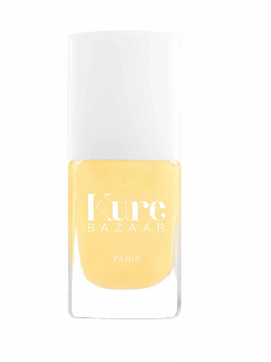 A bottle of Kure Bazaar Paris nail polish in a soft pastel yellow shade, featuring a white cap and a clear glass base, set against a plain white background.